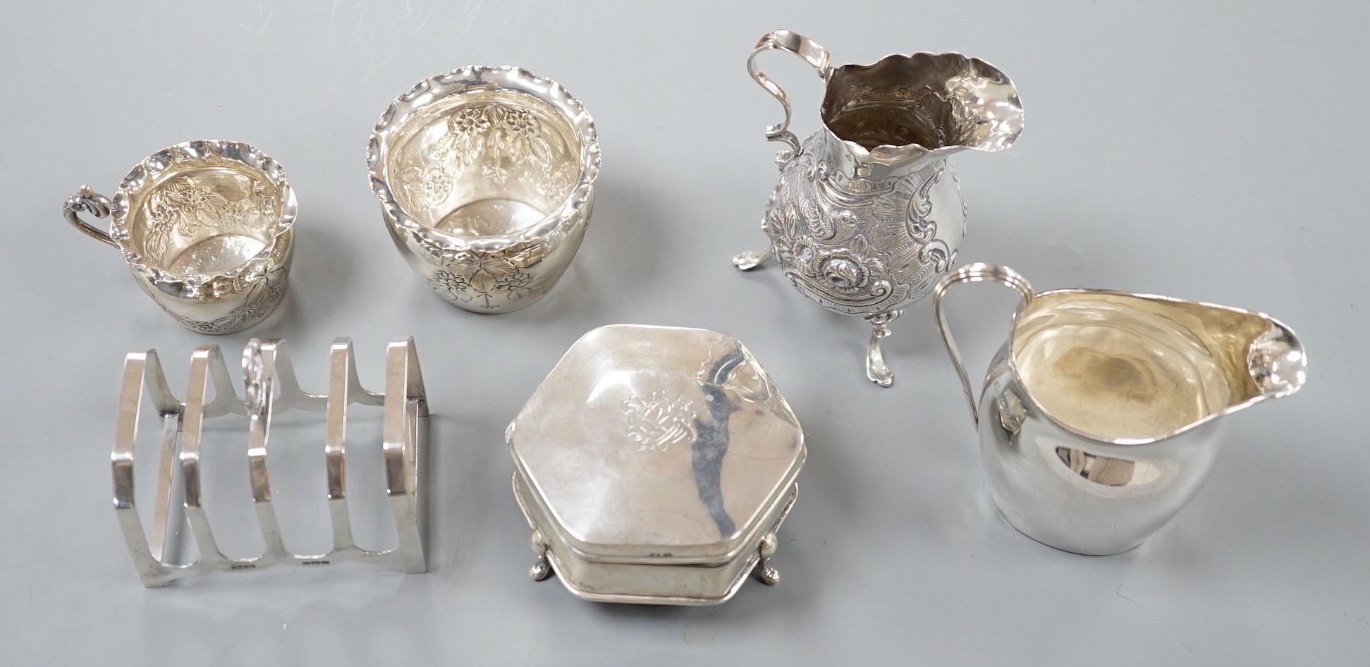 An Edwardian repousse silver bachelors cream jug and sugar bowl, Birmingham, 1904, two other late 19th/early 20th century silver cream jugs, a silver five bar toastrack and a silver mounted trinket box.